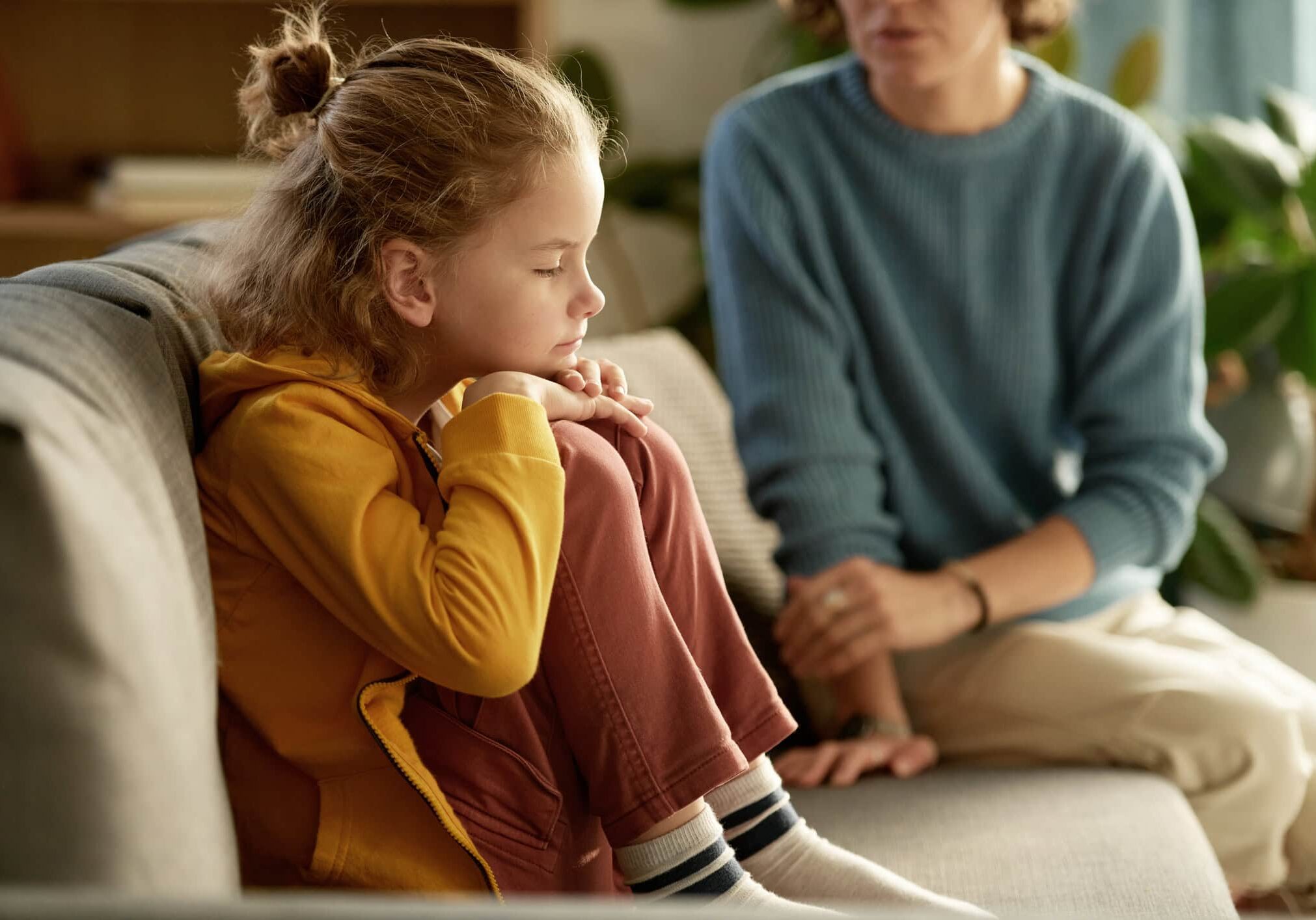 Little boy sitting on sofa without mood and having no desire to talk to his mom