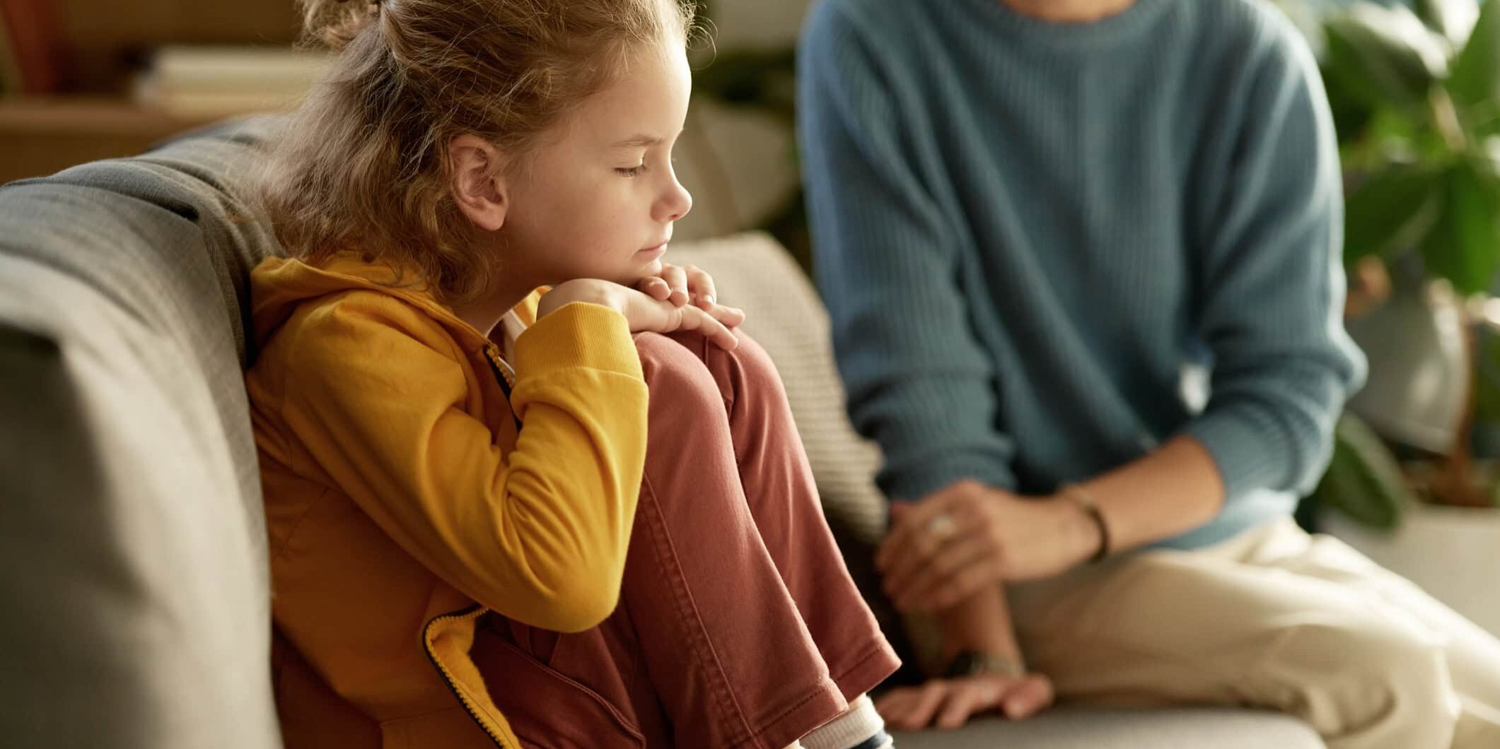 Little boy sitting on sofa without mood and having no desire to talk to his mom